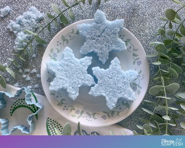 three blue snowflake-shaped bath salt cakes sitting on a plate