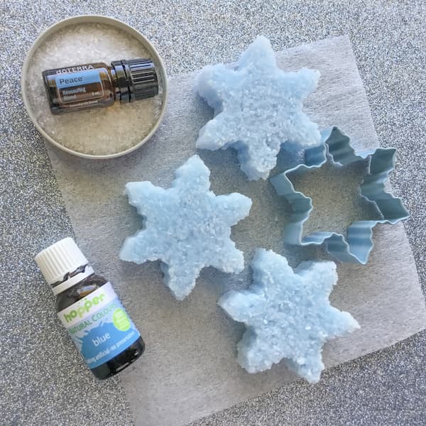 blue bath salt cakes laid out with a bottle of doterra Peace essential oil, a bottle of blue food colouring, and a snowflake-shaped cookie cutter