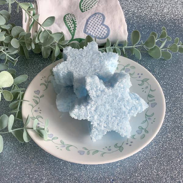 three blue snowflake-shaped bath salt cakes stacked on a plate