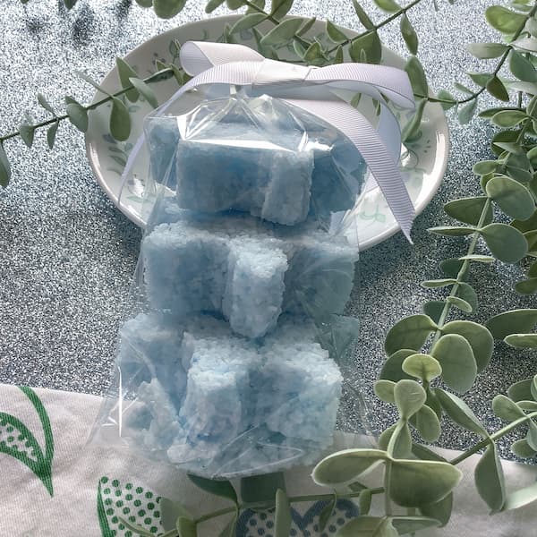 three blue snowflake-shaped bath salt cakes in a clear cellophane bag with a white ribbon on top
