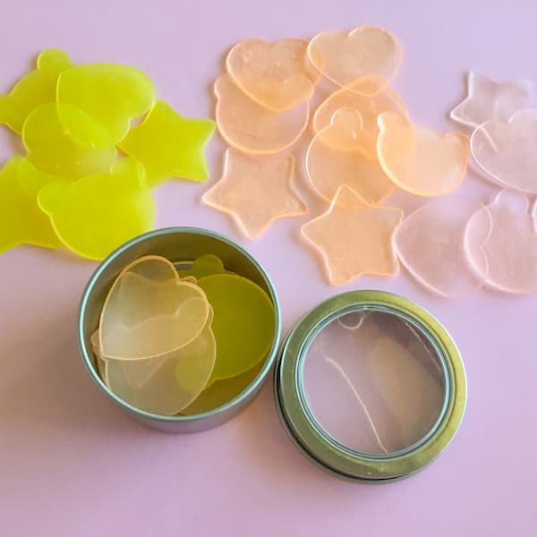 super thin pink, orange and yellow melt and pour soap bars laid out on a pink background.  some of the soaps are in a round metal tin.