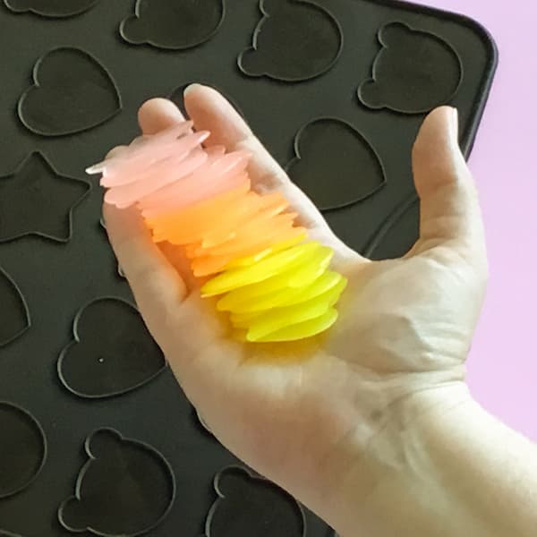 an out-stretched hand holding a collection of pink, orange, and yellow single use soap bars