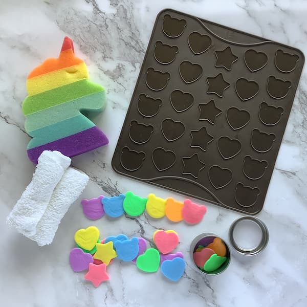 rainbow coloured single use soaps laid out with a rainbow unicorn sponge and a silicone macaron mat