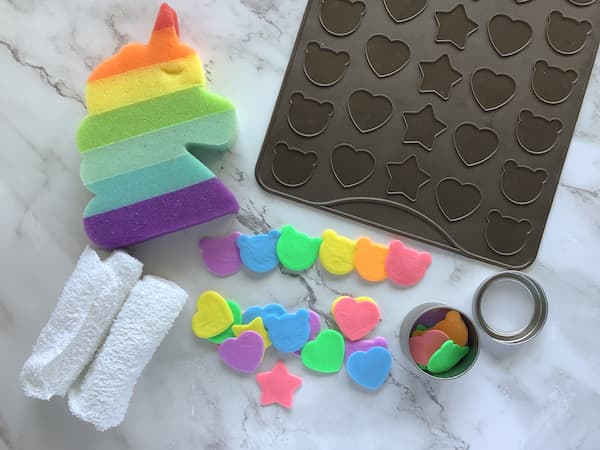 rainbow coloured single use soaps laid out with a rainbow unicorn sponge and a silicone macaron mat