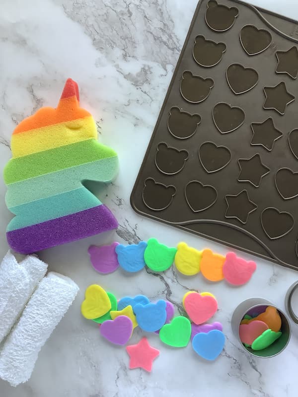 rainbow coloured single use soaps laid out with a rainbow unicorn sponge and a silicone macaron mat