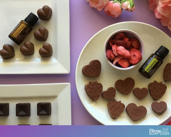 valentine's chocolates laid out on plates with flowers, freeze dried strawberries, a heart silicone mold and bottles of doterra essential oils