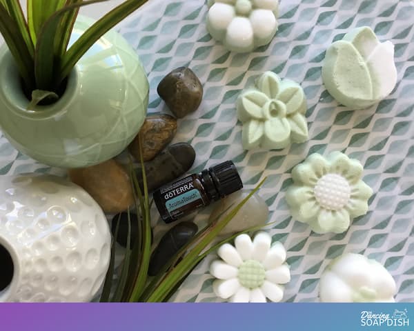 green and white floral bath bombs surrounded by rocks and grass with a bottle of doterra aromatouch essential oil