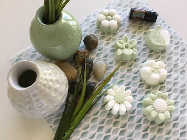 green and white floral bath bombs surrounded by rocks and grass with a bottle of doterra aromatouch essential oil