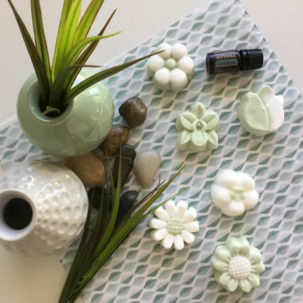 green and white floral bath bombs surrounded by rocks and grass with a bottle of doterra aromatouch essential oil
