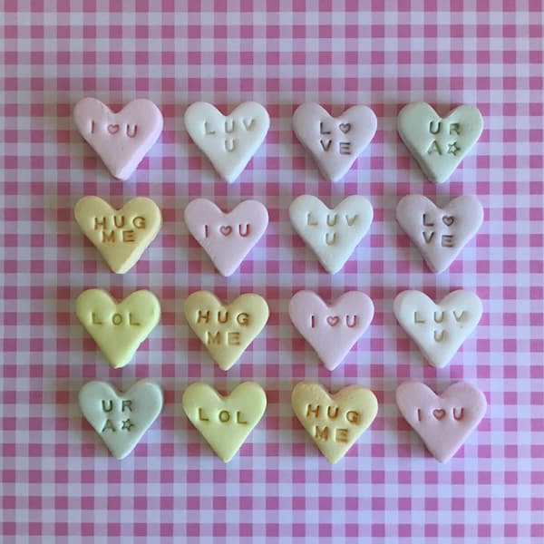 green, pink, yellow, orange, purple and white conversation hearts laid out in a grid on pink gingham backdrop