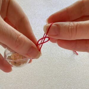 a pair of hands tying a looped piece of thread to a bauble