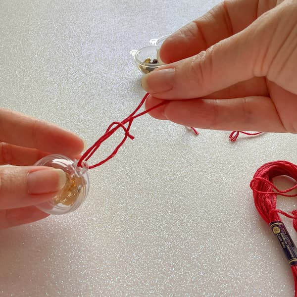 a pair of hands tying a looped piece of thread to a bauble