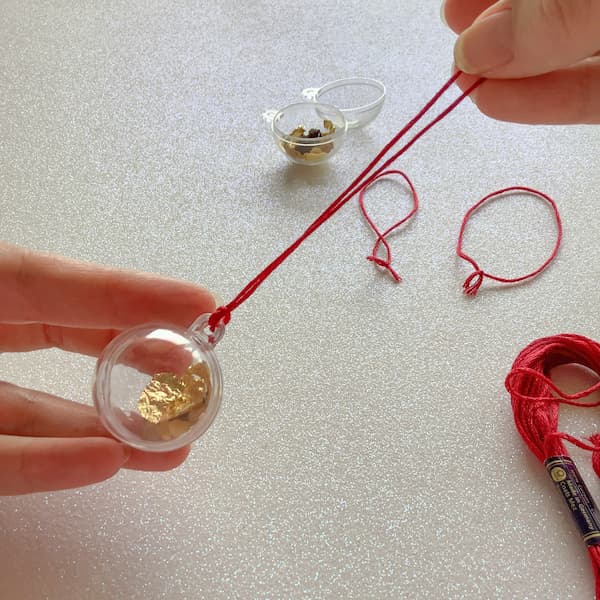 a pair of hands holding a bauble with a looped hanging thread attached
