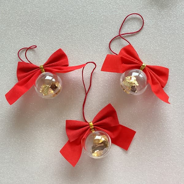 three clear baubles filled with gold, frankincense and myrrh with a red velvet bow on top