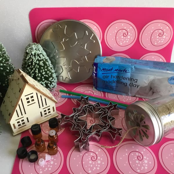 essential oil sample vials, drinking straws, snowflake cookie cutters, white air-hardening clay and craft string laying on ikea silicone baking mat