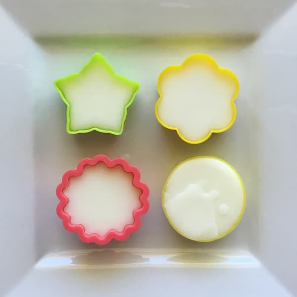 four recently poured essential oil lotion bars in four floral molds laid out on a square plate to set