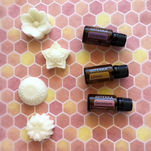 four floral essential oil lotion bars laid out next to bottles of doterra lavender, doterra litsea, and doterra geranium essential oils
