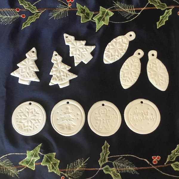 white clay essential oil diffuser ornaments made with christmas cookie cutters and stamps laid out on a navy blue table runner with metallic christmas embroidery