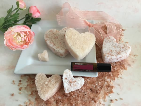 heart-shaped pink himalayan bath salt cakes laid out on a plate with a bottle of doterra rose touch