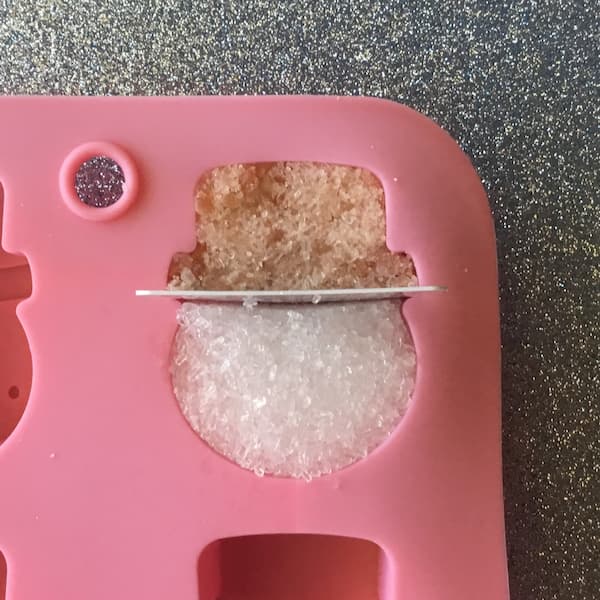 a plastic library card stuck through the middle of a mold cavity to separate a pink himalayan salt hat from an epsom salt face