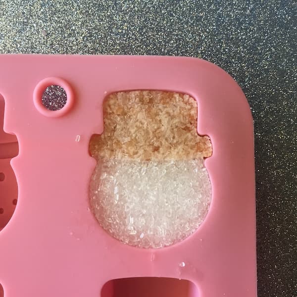 a snowman mold cavity filled with two different bath salt mixtures: white for the face and pink for the hat