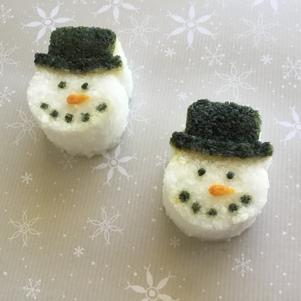 five snowman bath salt cakes laid out on a blue board with two candy canes positioned in the shape of heart