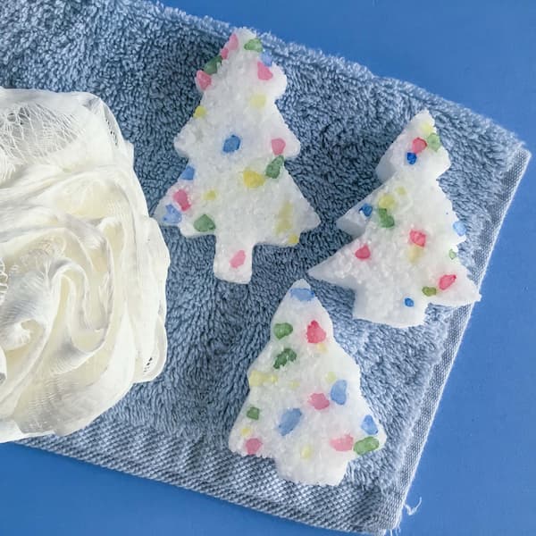 Christmas tree bath salt cakes sitting on a blue face washer with a loofa