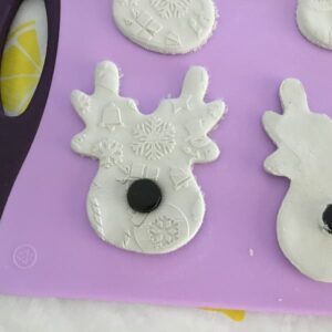a reindeer shaped white clay cut out with a black cap pushed into the clay where the nose would be