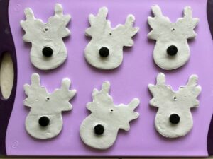 white clay reindeer faces with caps for noses laid out on a purple board