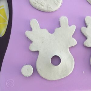 a white clay reindeer face with a hole punched out where the nose would be