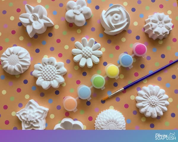 plaster of paris flowers on an orange background with a paintbrush and assorted coloured craft paints