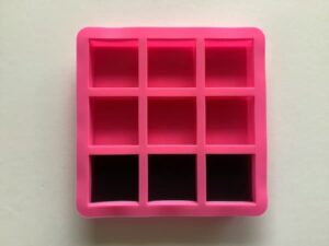 a nine-cavity square soap mould, three cavities of which are filled three quarters of the way with black soap