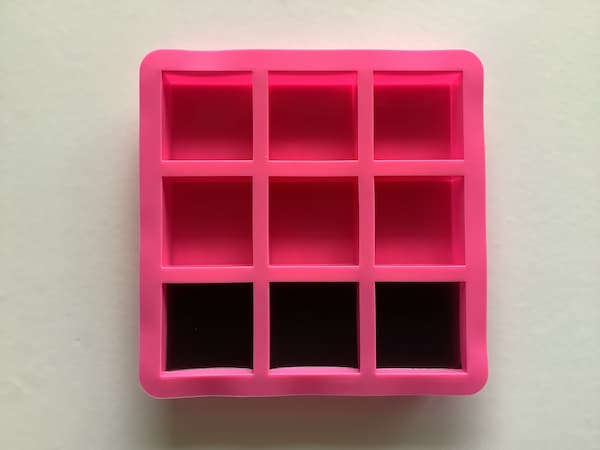 a nine-cavity square soap mould, three cavities of which are filled three quarters of the way with black soap