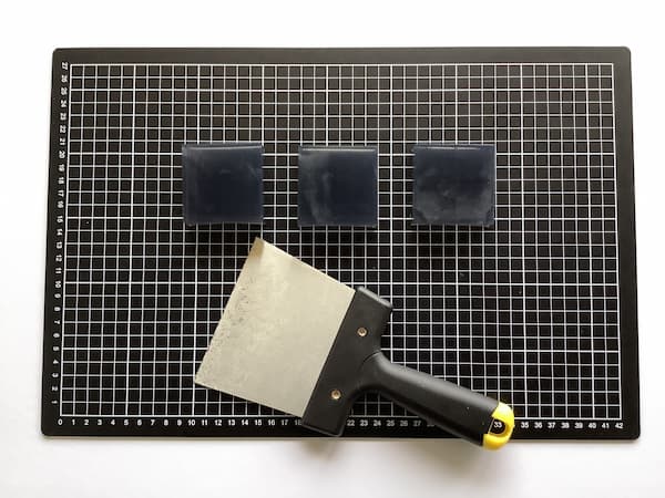 three square bars of black soap sitting on a cutting mat with a large paint scraper