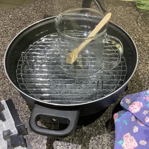 a 500ml glass jug filled with melted clear soap base sitting in an electric frypan filled with water