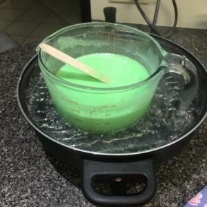 a 1L glass jug filled with melted green soap base sitting in an electric frypan filled with water