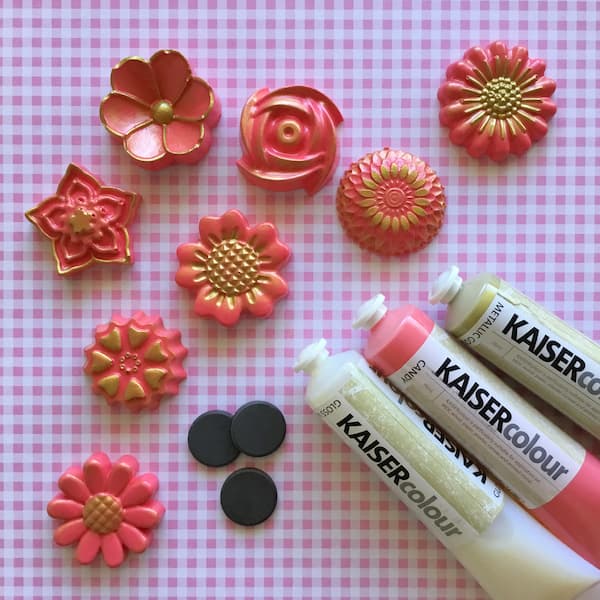 floral fridge magnets on a pink gingham background with a pile of craft magnets and three tubes of acrylic paint