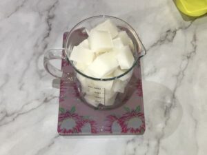 a glass jug filled with cubes of white melt and pour soap base sitting on a set of kitchen scales