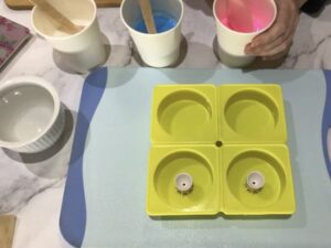 a four-cavity circular silicone mould with two paint pouring tools sitting in the centre of two of the mould cavities