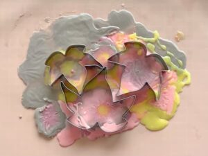 blobs of pink, orange, yellow and brown melt and pour soap base on a silicone baking mat with three leaf shaped cookie cutters pressed into the soap