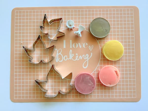 a peach coloured silicone baking mat with three maple leaf shaped cookie cutters and four circular blocks of melt and pour soap coloured brown, yellow, orange and red