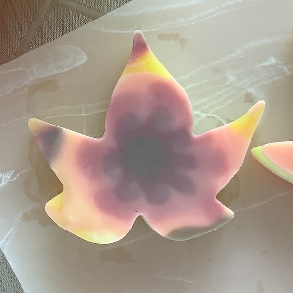 a maple leaf shaped soap bar decorated with a tie dye effect in four autumn colours - brown, red, orange and yellow.
