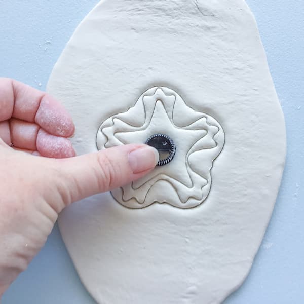 a thumb pressing down on a black essential oil vial cap in the centre of a wet clay diffuser design