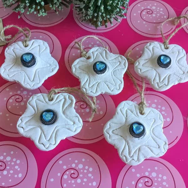 five white clay diffuser ornaments with essential oil vials embedded in the centre. each black vial cap has a blue heart gem stuck to it.