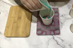 pouring green melt and pour soap into a paper cup with a cookie stamp inside it