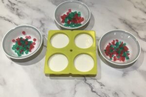 a four-cavity round soap mould filled with white soap bars surrounded by three bowls each with mosaic tiles of different shapes in them