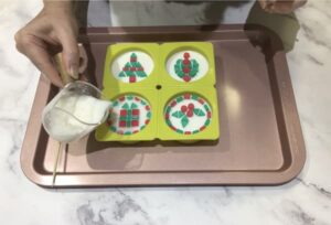 a hand pouring white soap base around coloured mosaic soap tiles