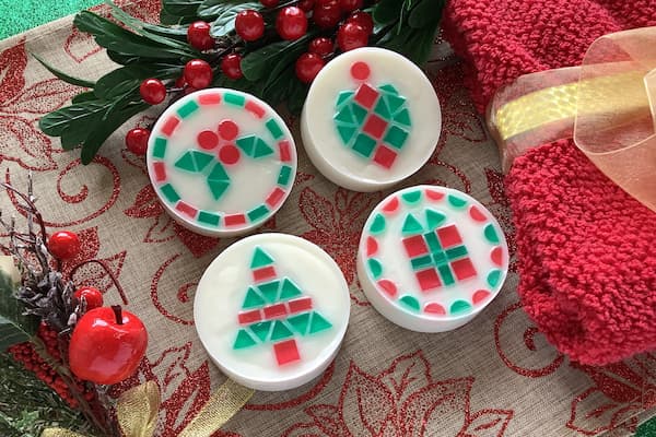 four Christmas themed mosaic soap bars displaying holly, ornament, Christmas tree, and Christmas gift designs