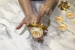 a pair of hands holding a gold-stamped nativity ornament