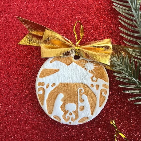 a round clay ornament embossed with a nativity scene and a gold bow